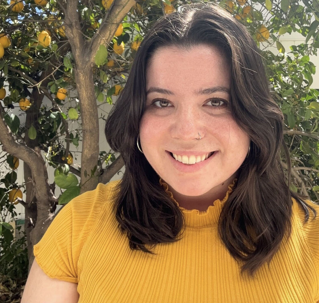 Headshot of Research Assistant Hannah Serrano wearing a yellow shirt and standing in front of a lemon tree. 